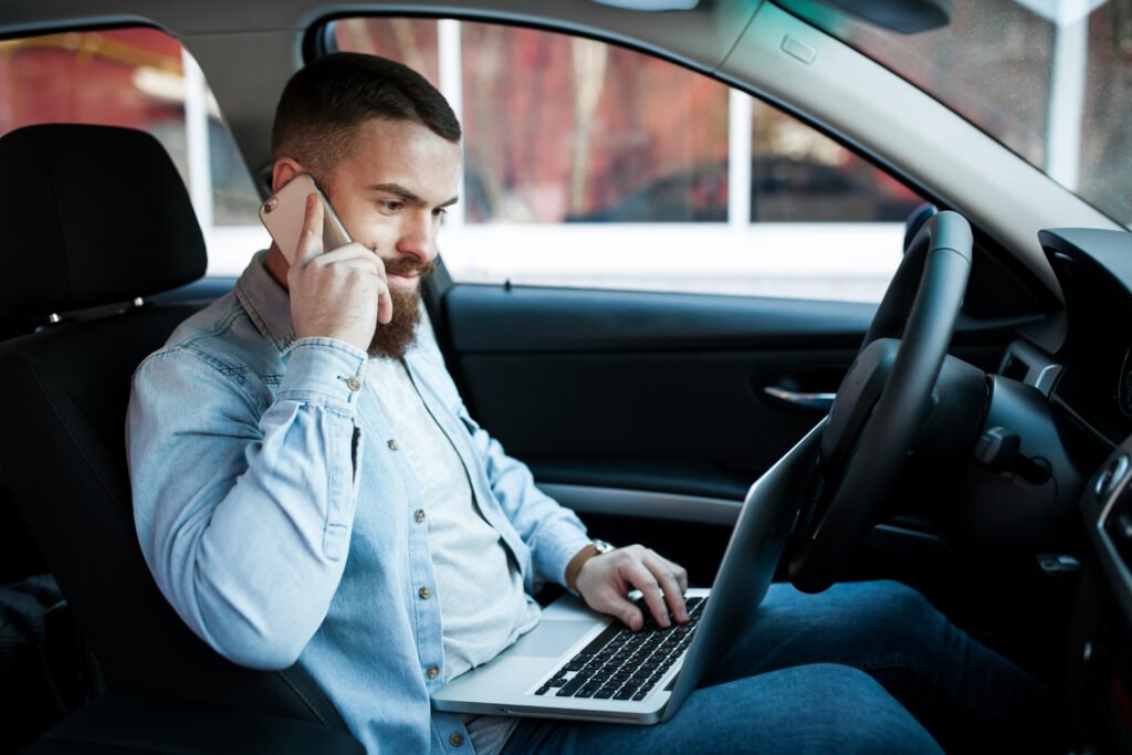 A man in the driver's seat of a car, working on his laptop, showcasing a rental car service in Dubai.