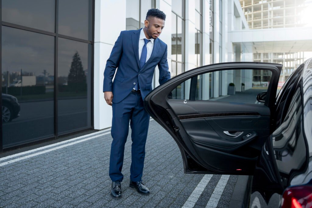 A suited man steps out of a car, showcasing a luxury chauffeur service in Dubai.jpg