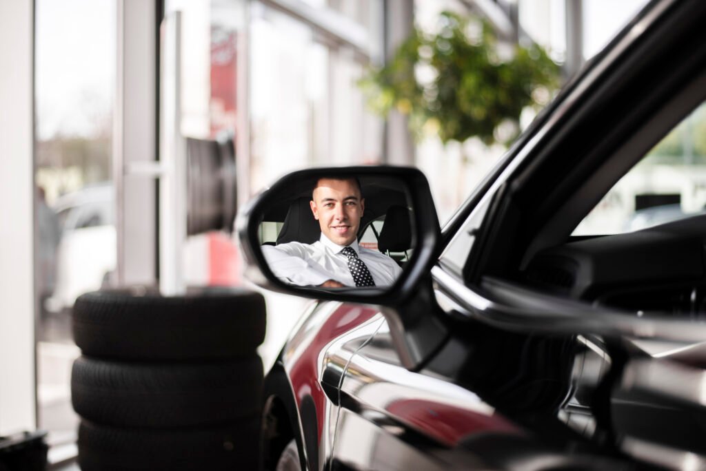 A man in a suit gazes at his reflection in a car's rearview mirror while driving in Dubai.jpg